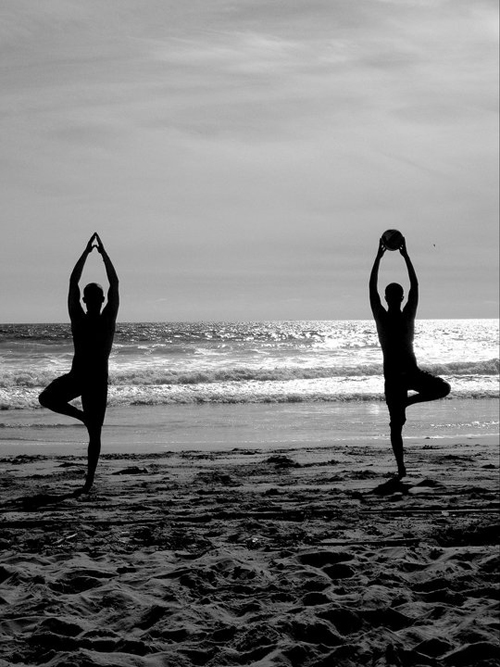 two people standing in mirror positions at the beach