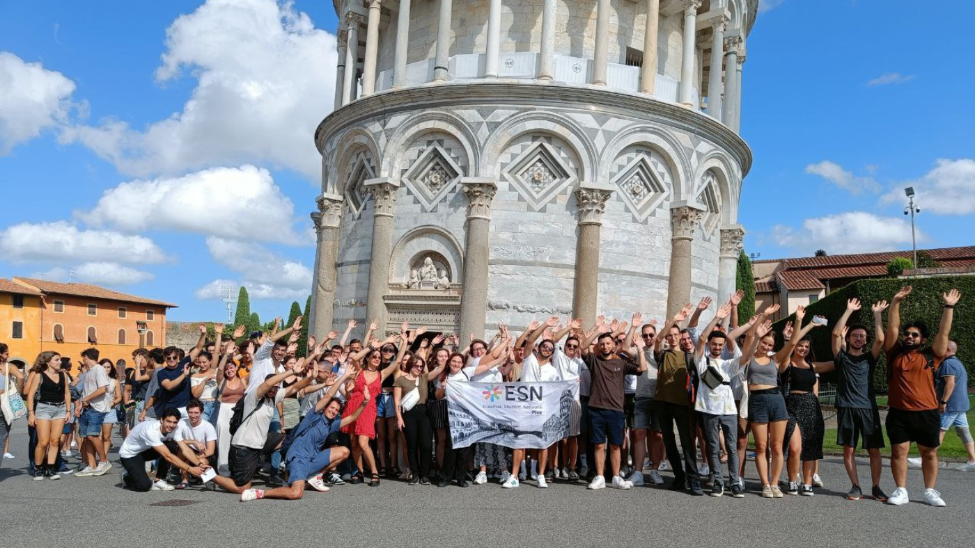A big group of people posing for a photo in front of the Leaning Tower of Pisa.